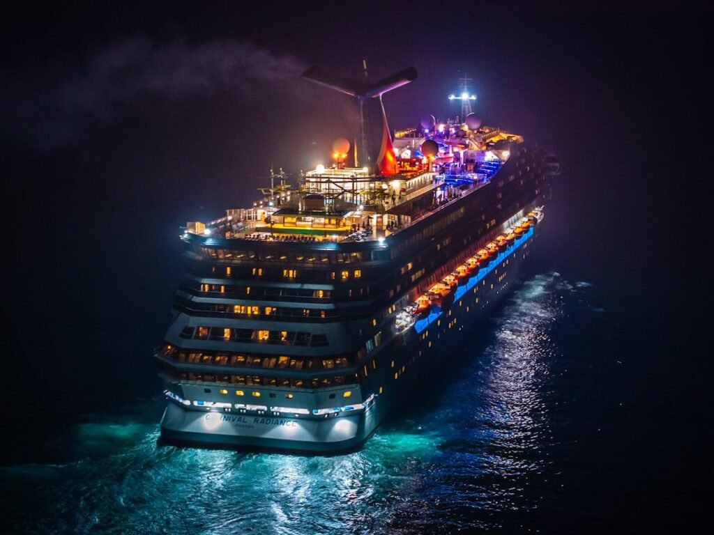 A vividly lit cruise ship sails through dark waters at night, creating a striking contrast.