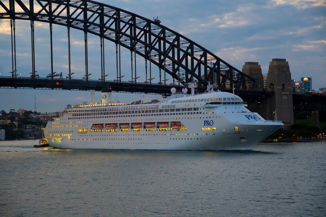 Elegant cruise ship navigates under Sydney's iconic Harbour Bridge at twilight.